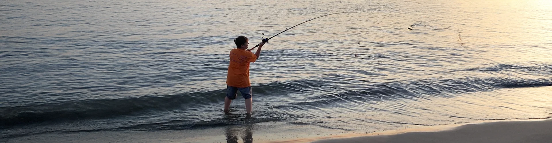 Standing in the water, a man uses surf fishing gear rental Charleston from Charleston Fishing Rentals.