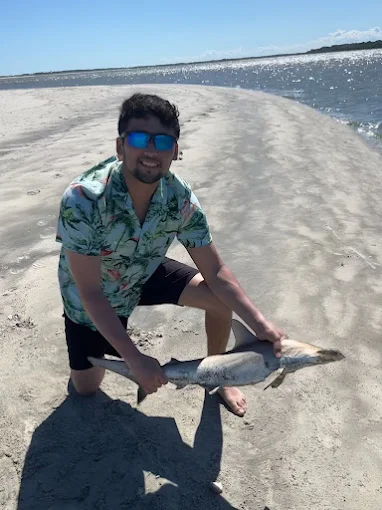 Kneeling with a catch, a man uses fishing rod and reel rental Charleston from Charleston Fishing Rentals.