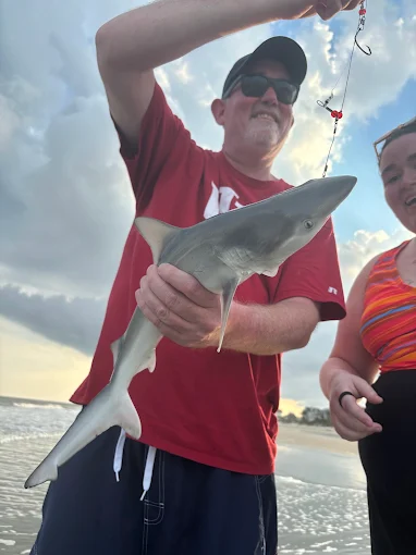 A couple holding a shark uses shark fishing gear rental Charleston from Charleston Fishing Rentals in Isle of Palms, South Carolina.