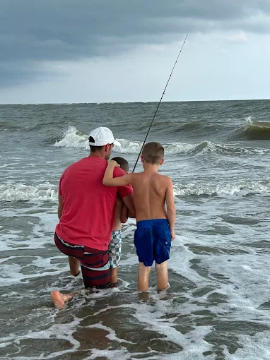 Two boys fishing in the ocean use surf fishing gear rental Charleston from Charleston Fishing Rentals.