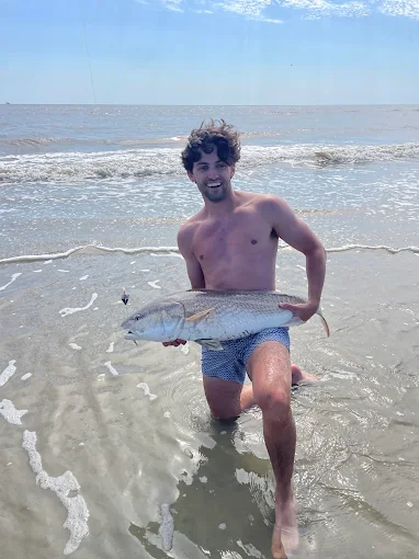 Holding a catch on the beach, a man uses fishing rod and reel rental Charleston from Charleston Fishing Rentals.